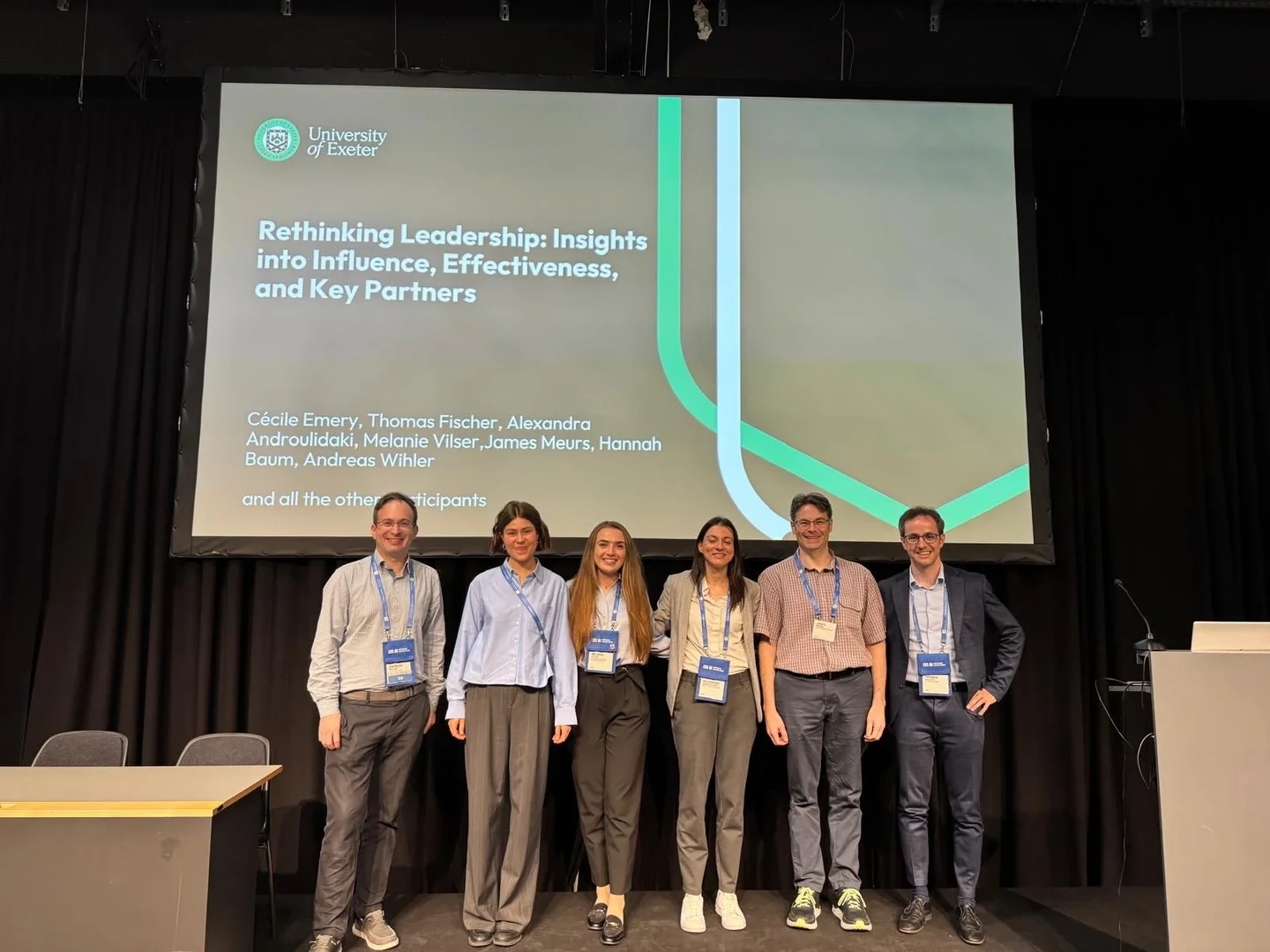 Eine Wissenschaftlerin und ein Wissenschaftler arbeiten hinter einer Glasfassade und mischen Chemikalien mit Großgeräten.